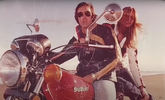 Nando y Veronique sobre una moto Suzuki roja, años 80.png